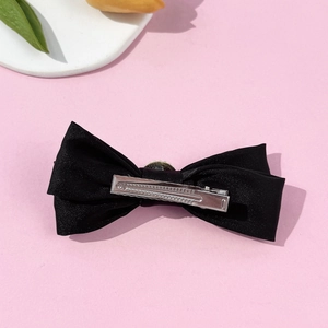 Elegant black satin bow hair clip with silver duckbill clip on a soft pink background