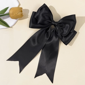 Detail view of large black satin bow hair clip with long ribbons on a cream background