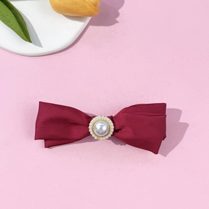 Detail of burgundy satin bow hair clip with a centered white pearl decoration
