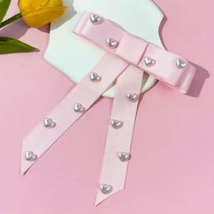 Detail of pink satin bow hair clip with silver heart beads on a soft pink background