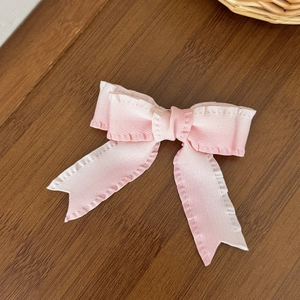 Close-up of pink and white ruffled ribbon bow hair clip on a textured wooden background