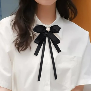 Detail of a black satin ribbon bowknot brooch with pearl and rhinestone on a white shirt