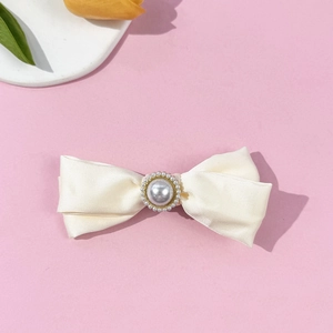 Detailed close-up of cream satin bow hair clip with central pearl and gold metal setting