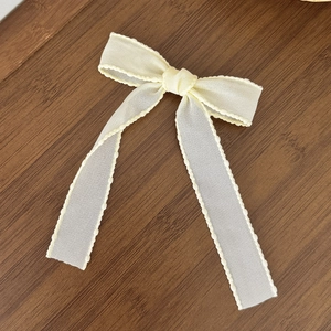 Detail of a creamy yellow ribbon hair clip with wavy scalloped edges on a wooden surface