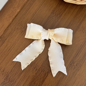 Detailed close-up of cream-colored bow hair clip showing textured fabric on wood background