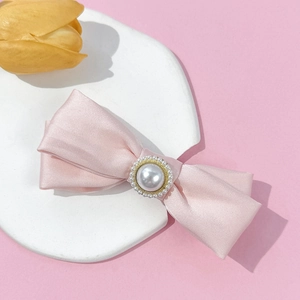Close-up of pink satin bow hair clip featuring a large central pearl with gold accents
