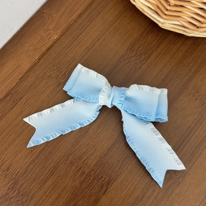 Detailed view of a gradient blue bow hair clip with ribbed texture on wood background