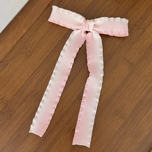 Detailed macro view of pink ribbon bow hair clip with ruffled lace edges on wooden texture