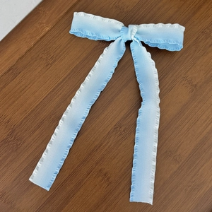 Detail of light blue gradient bow hair clip with pleated chiffon fabric on wood background