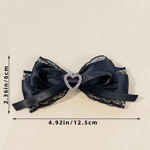 Detalle de lazo de encaje negro con diamante de corazón y medidas de 12,5 x 6 cm
