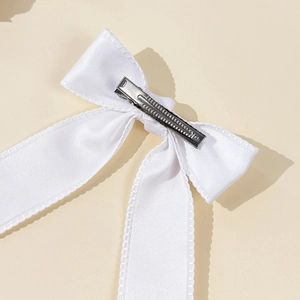 Elegant white satin bow hair clip with silver metal alligator clamp on a beige background