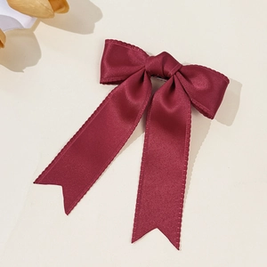 Close-up of burgundy satin bow hair clip with long ribbons and elegant wavy scalloped edges