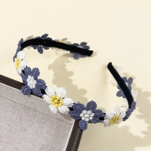 Dettaglio del ricamo a margherita bianco e blu sul cerchietto per capelli nero