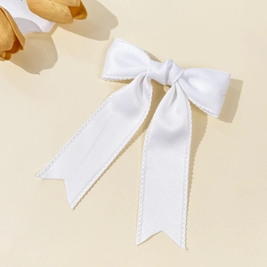Detail of white silk bow hair clip with lace edges and long ribbons on warm background