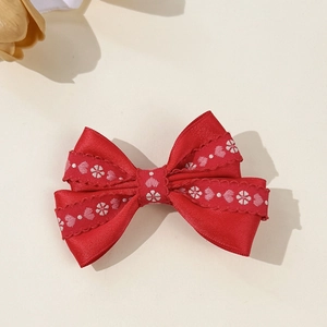 Détail d'une pince à cheveux avec nœud en satin rouge et broderie de fleurs et de cœurs