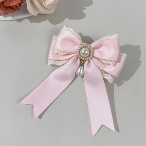Detailed macro view of pink satin bow hair clip with lace trim and pearl pendant drop