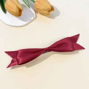 Detailed macro view of a burgundy satin silk ribbon bow hair clip on a beige surface