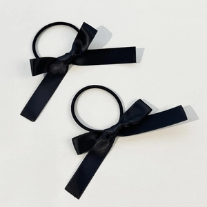 Detail view of two black satin bow hair ties with long ribbons on a plain white surface