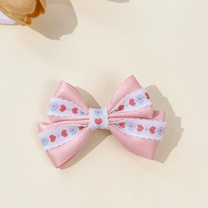 Détail d'une pince à cheveux avec nœud en satin rose, dentelle et broderies de cœurs