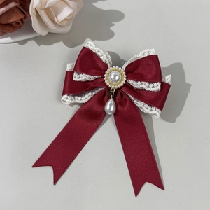 Macro detail of wine red satin bow hair clip with white lace edges and pearl pendant