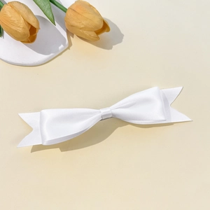 Detail of white satin ribbon bow hair clip with swallowtail ends on a minimalist backdrop
