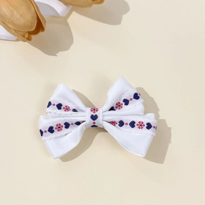 Détail d'une pince à cheveux nœud blanc avec broderie fleurie et cœur et bords ondulés