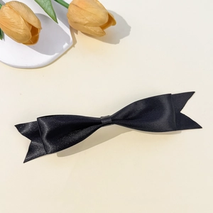 Detail of elegant black satin bow hair clip with glossy texture on a minimalist background