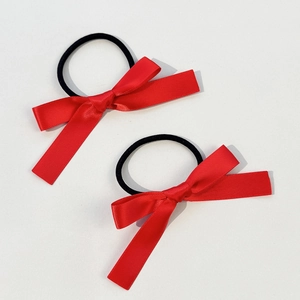 Close-up of two red satin bow hair ties with black elastic bands on cream background