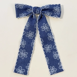 Détail d'un nœud en denim bleu avec broderie de marguerites blanches et bordure festonnée