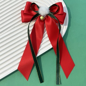 Detail of red Christmas bow hair clip with plush white ball and gold bell on a plate
