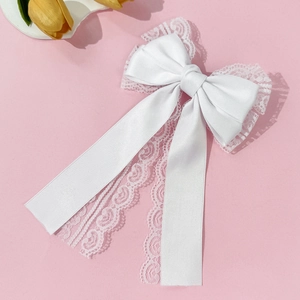 Close-up of white lace bow hair clip with satin ribbons on pink background