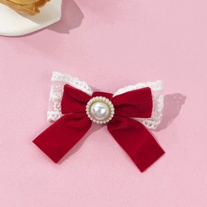 Detailed close-up of velvet red bow hair clip with white lace trim and center pearl decoration