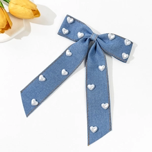 Détail du nœud en denim bleu avec perles en forme de cœur et coutures orange fines