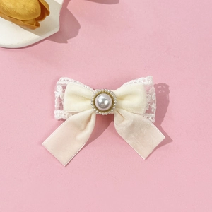 Detail of velvet bow hair clip with central pearl and delicate lace trim on pink surface