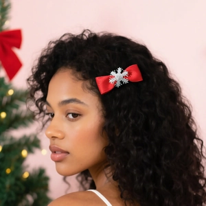Christmas red bow hair clip with silver snowflake shown on model with holiday tree background