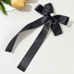 Detail of a black satin bow hair clip with a central pearl and long elegant ribbon tails