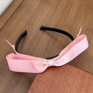 Close-up of pink satin bow headband with elegant silk texture and black fabric wrap