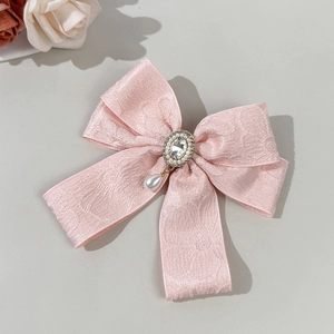 Close-up of pink jacquard bow hair clip with rhinestone center and teardrop pearl pendant