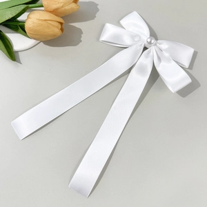 Detailed close-up of white satin bow hair clip with pearl center and long ribbons