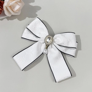 Detail of white jacquard bow hair clip with rhinestone center and teardrop pearl pendant
