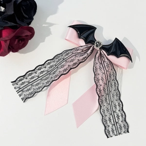 Nahaufnahme der rosa Schleife mit schwarzer Spitze, Fledermausflügeln und Herzstein