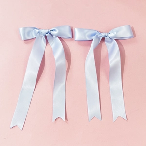 Detail of light blue satin hair clips with long ribbon streamers on pink background