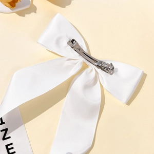 Elegant white satin bow hair clip with long lettered ribbons and silver metal spring clip