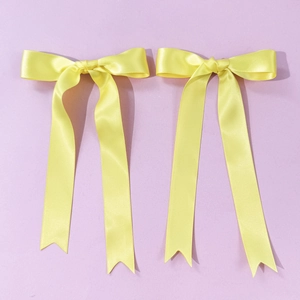 Detailed close-up of yellow satin ribbon hair clips with long streamers on purple background