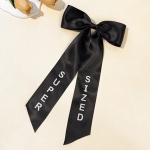 Detail of elegant black satin bow hair clip with white SUPER SIZED text on long ribbons