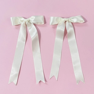 Close-up of a pair of cream satin ribbon hair bows with long swallowtail streamers