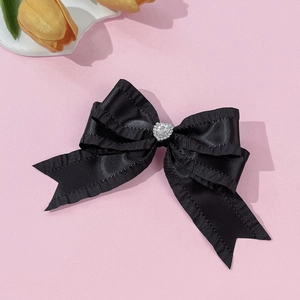 Détail du nœud papillon en satin noir avec bords volantés et un strass en forme de cœur