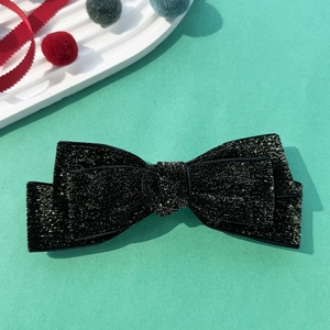 Detail of elegant black velvet bow hair clip with shimmering gold glitter on mint background