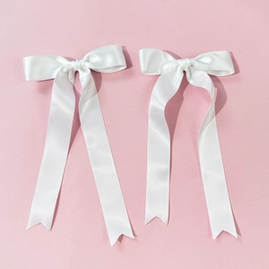 Detail of white satin bow hair clips with long ribbons on pink background