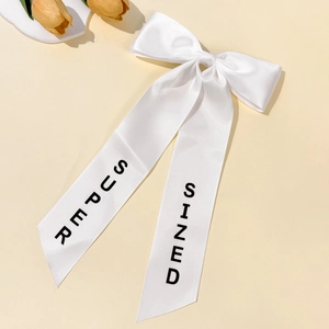 Detail of white satin bow hair clip with long ribbons and black SUPER SIZED print